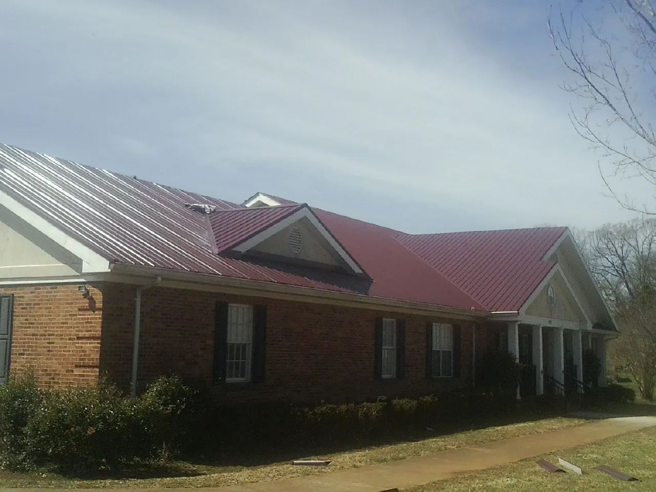 Red metal roof with gabled entries on a long brick building, from a Hail Damage Roof Repair job in Cayuga