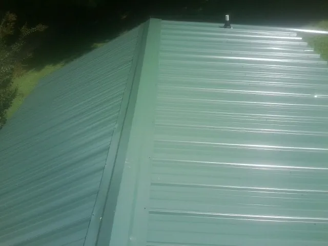 New green metal panels meeting at the ridge of a roof — Flat Roof Repair work by our crew in Cayuga