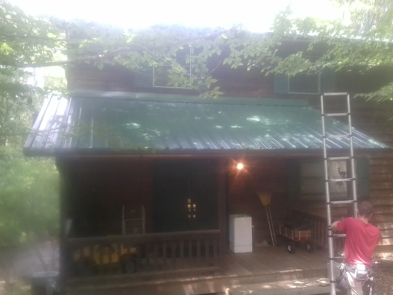 Worker on a ladder at the green porch roof of a wooded cabin in Cayuga