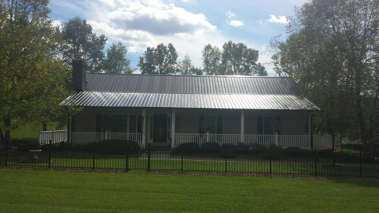 Gray metal roof on a brick ranch with a full width front porch — Gutter Guard Installation work by our crew in Cayuga