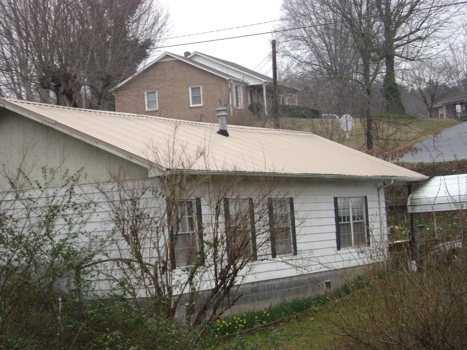 Tan metal roof on a white sided house set into a hillside — Commercial Roofing by Roofing Brothers in Cayuga